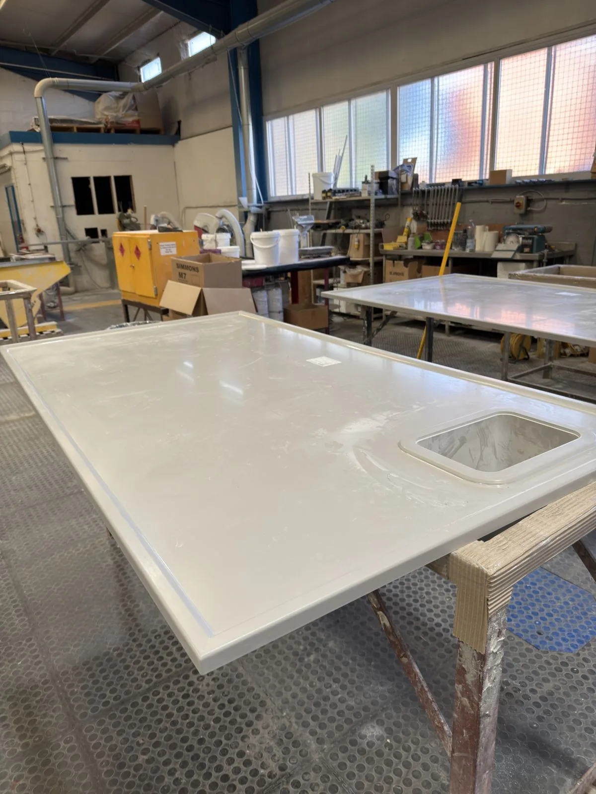 A white epoxy resin top with a raised edge and a small moulded sink, lying flat on trestles in the Simmons works